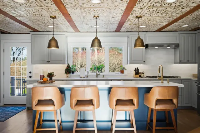 Modern kitchen interior featuring a large island with leather bar stools, decorative tin ceiling, and stylish pendant lighting, showcasing a recent renovation by Bradford Construction in Beverly, MA.