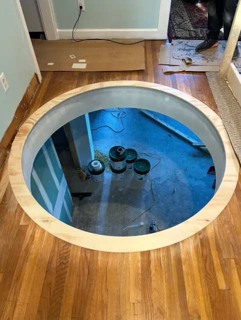 A round hole in the floor of a room with a wooden frame around it.