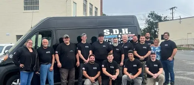 Group of people in black shirts pose in front of a black van with