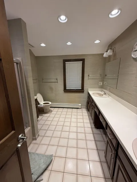 Bathroom with toilet, vanity, and window. Beige tile floor and textured walls.