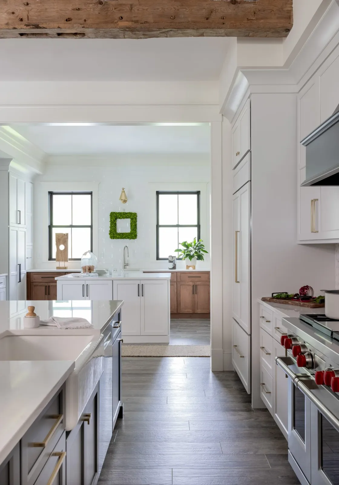 Bright modern kitchen with white and wood cabinetry, gray flooring, and two windows with black frames, decorated with green plants and minimalistic accessories.