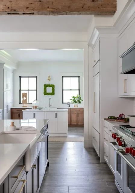 Bright modern kitchen with white and wood cabinetry, gray flooring, and two windows with black frames, decorated with green plants and minimalistic accessories.