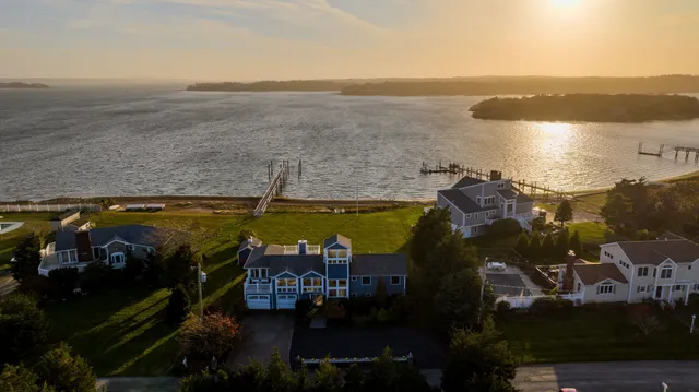 Aerial view of waterfront homes at sunset, featuring docks leading to the serene body of water and a warm, glowing horizon.