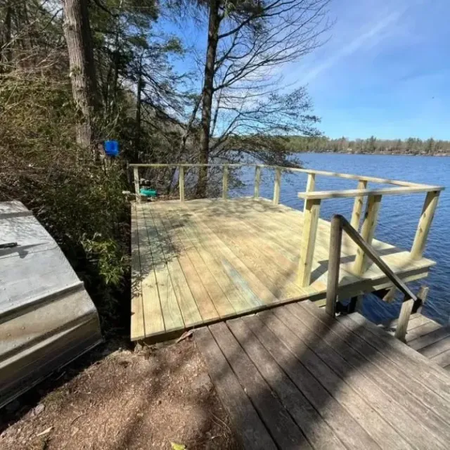 Wooden dock and deck beside a lake, with railing and trees on a sunny day