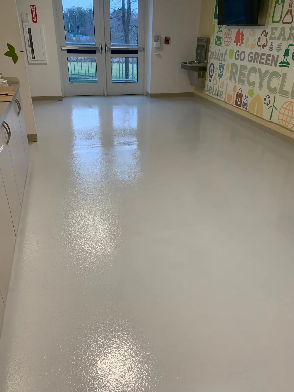 Empty school hallway with glossy white floor, colorful wall art, and glass doors at the end