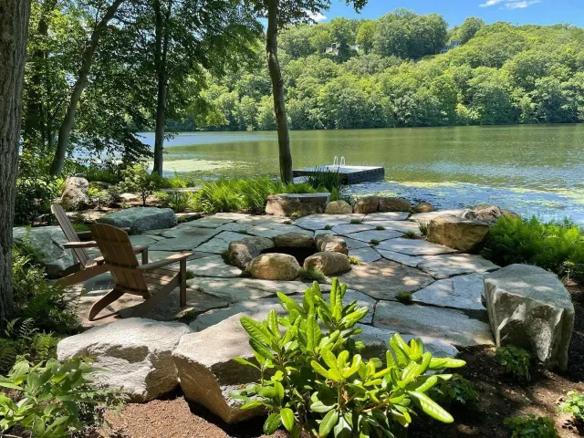 Granite fire put patio with boulders for seating and fern sod help make this cozy lakeside retreat in Branford, Connecticut.