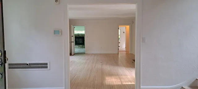 Interior hallway with white walls, wood floors, and a short step up to a brighter room beyond