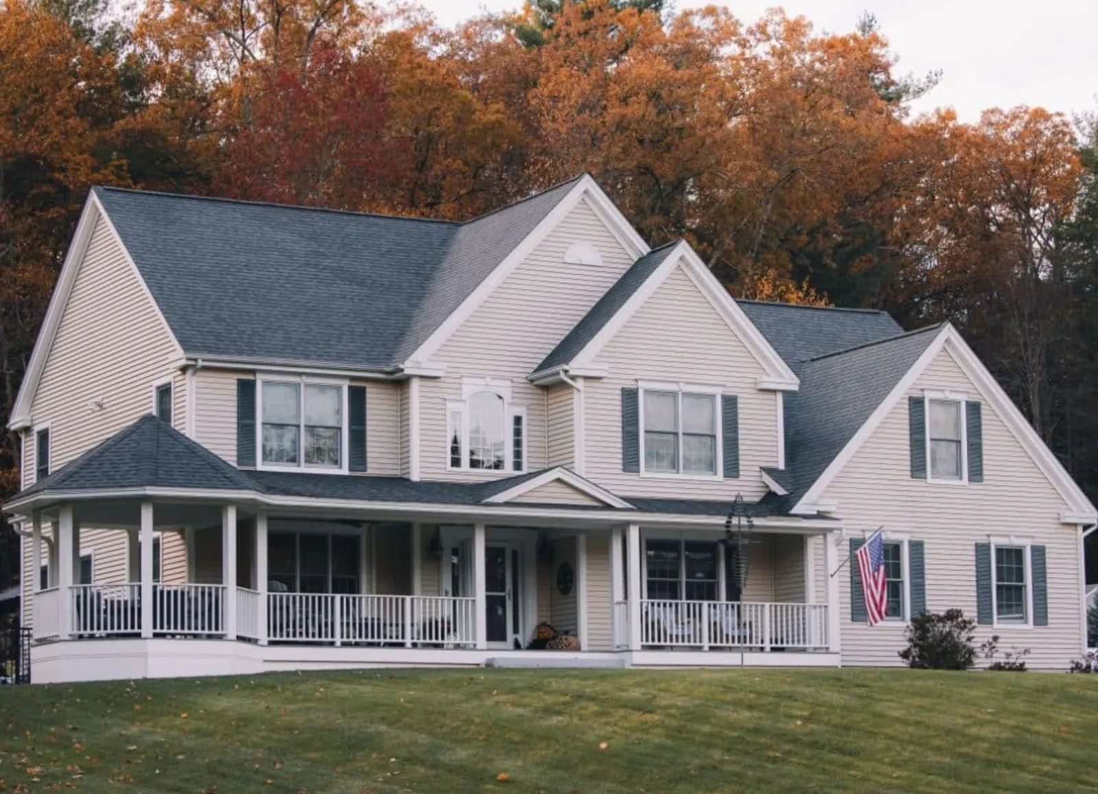 Beige two-story house with white trim, front porch, and American flag on a grassy lawn