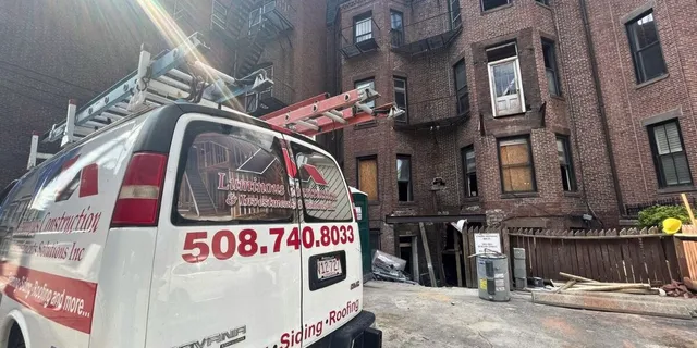 Luminous Construction service van parked outside a historic brick building restoration site in Massachusetts