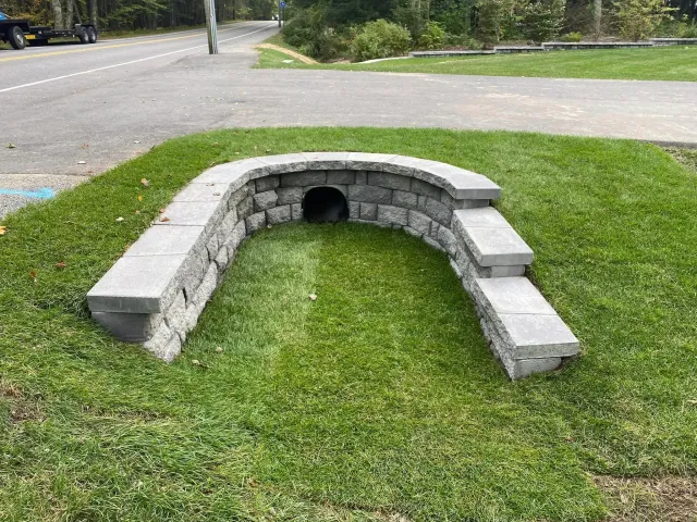A stone wall with a hole in the middle of it in the grass.