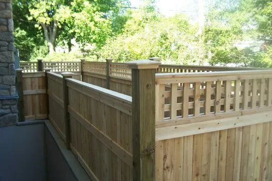 Wooden privacy fence along a narrow outdoor walkway beside a stone wall and trees