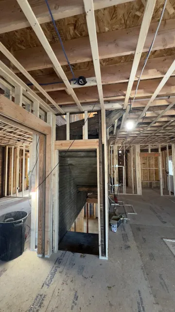 Interior view of a building under construction, showing wooden framing and stairwell.