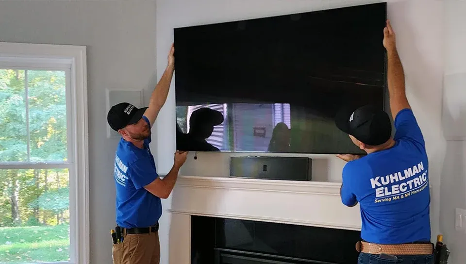 Kuhlman Electric electricians installing a wall-mounted TV above a fireplace.
