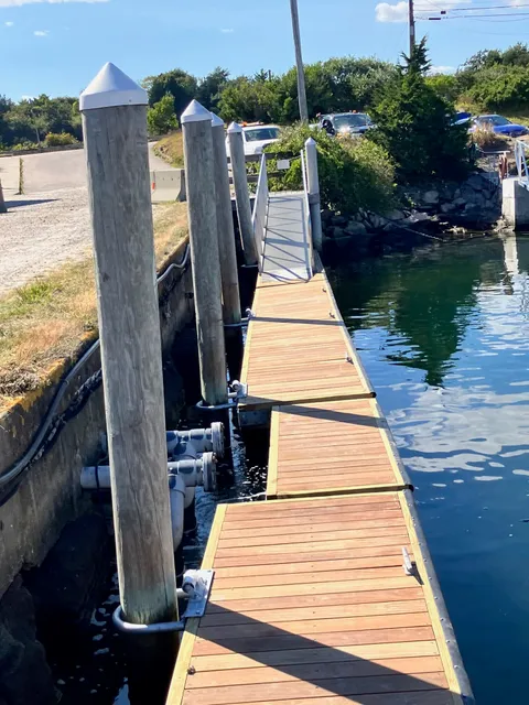 Waterfront dock and gangway with wooden planks, supporting posts, and calm water, showcasing a custom build project by Next Step Property Services in Southern New Hampshire.