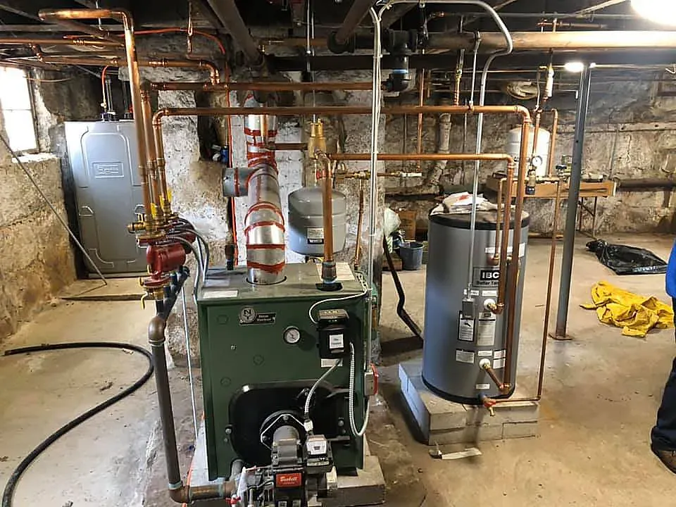 A green boiler is sitting in a basement next to a water heater.