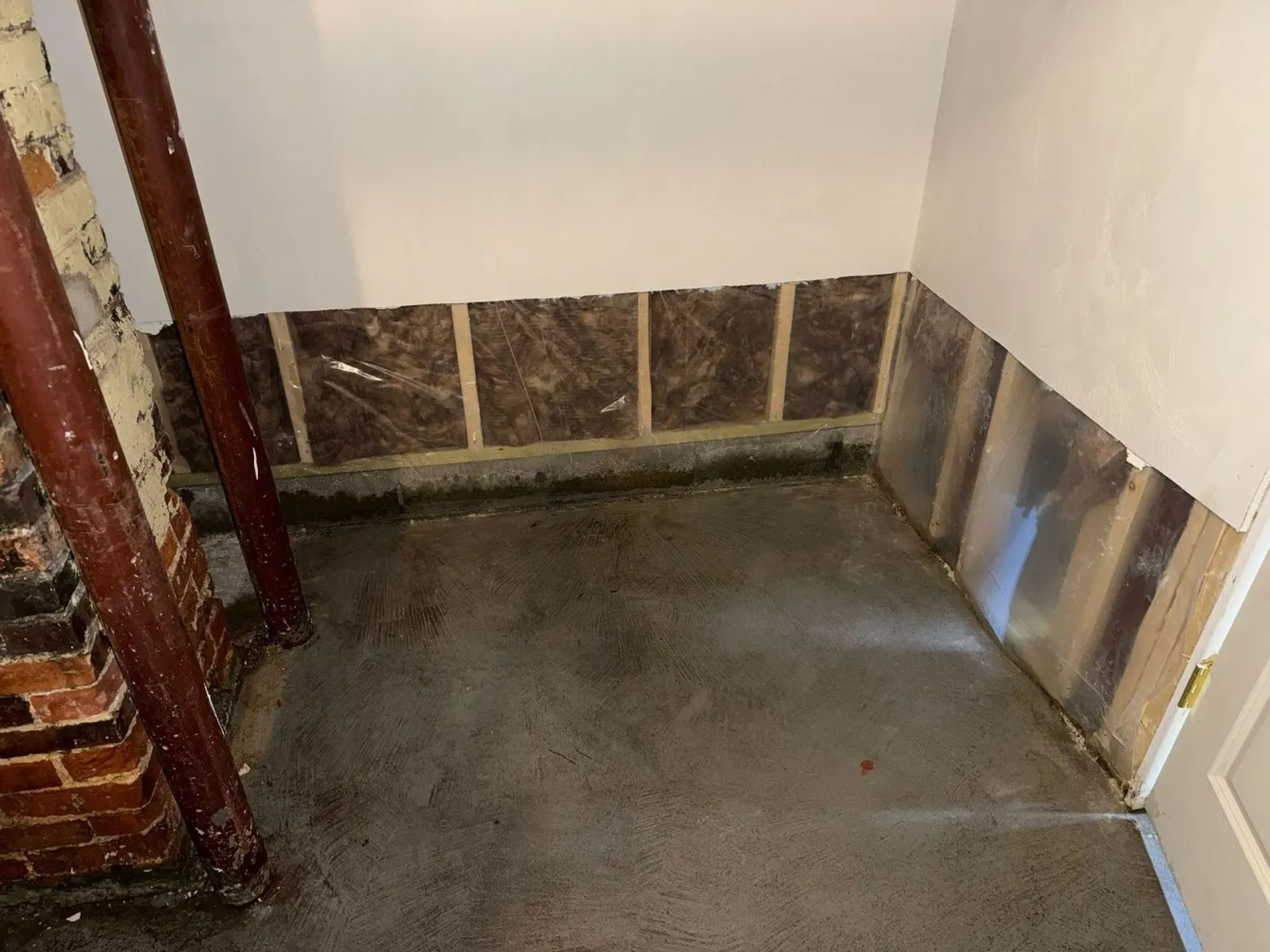Empty unfinished room corner with a dark concrete floor, white walls, and brown tile trim along the base.