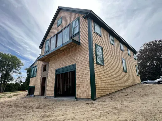 Two-story brick building with green trim and a steep roof, viewed from a low angle on a sandy lot.