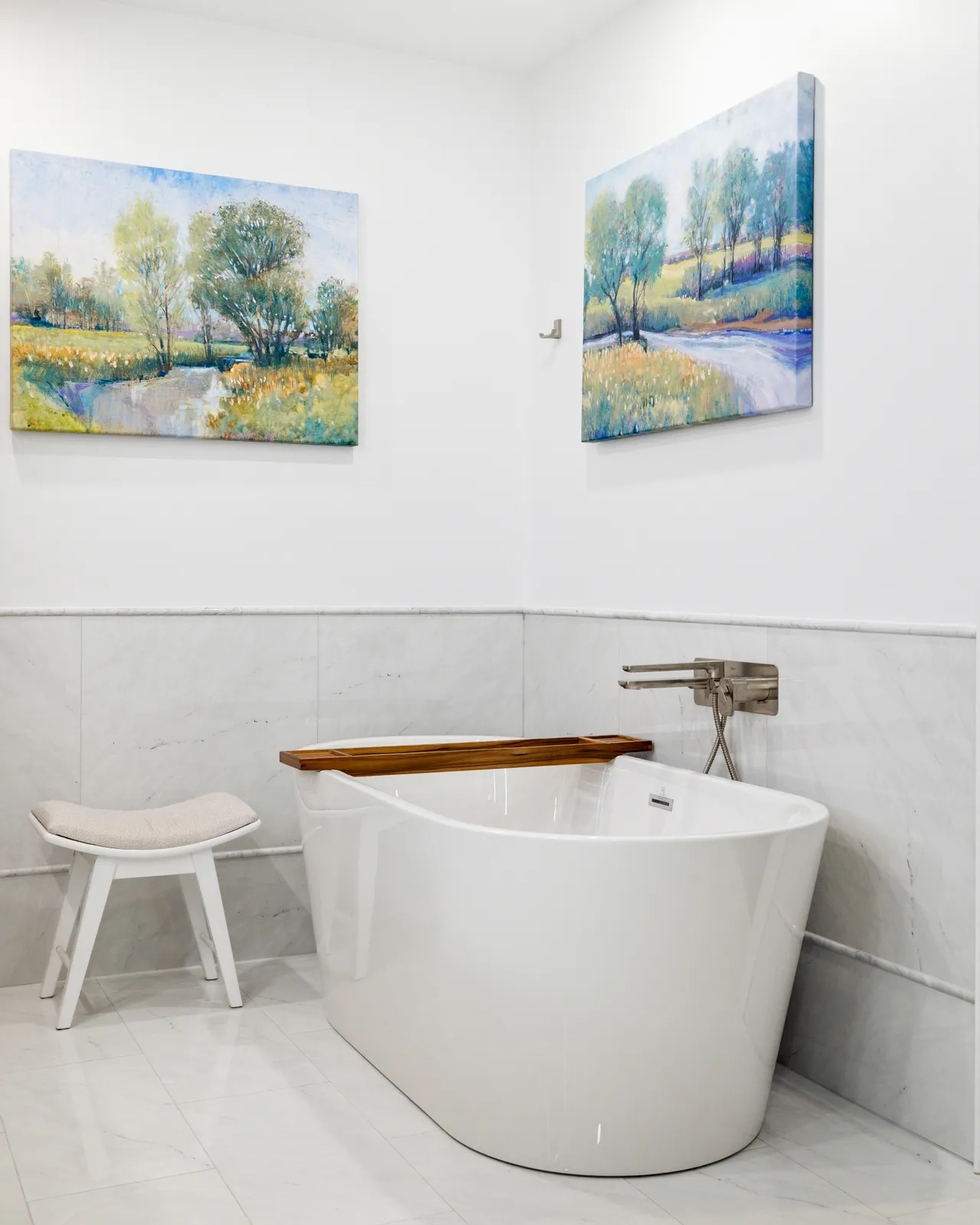 Freestanding soaking tub against marble-look tile in a Braintree primary bath, with a wall-mounted filler and a white stool.