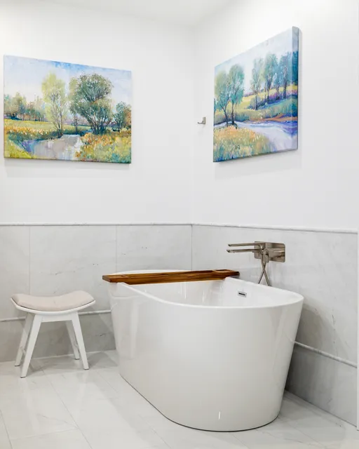 Freestanding soaking tub against marble-look tile in a Braintree primary bath, with a wall-mounted filler and a white stool.