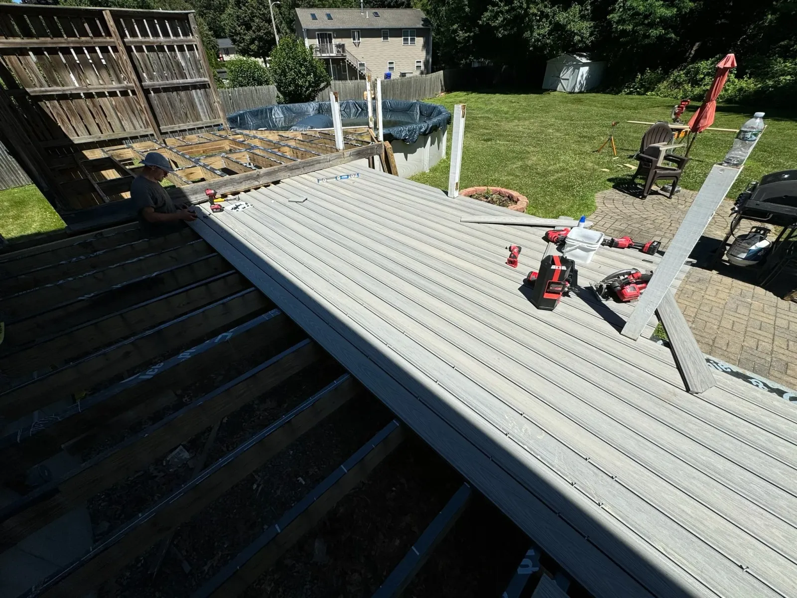 Construction worker installing a new wooden deck in a backyard with tools and equipment around.