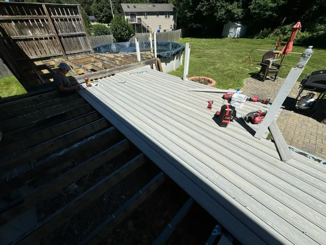 Construction worker installing a new wooden deck in a backyard with tools and equipment around.