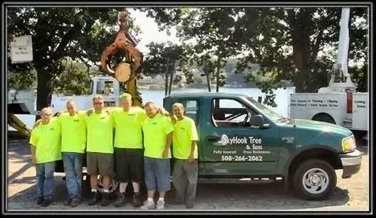 Skyhook Tree & Trim team posing beside a green truck in front of equipment and trees.
