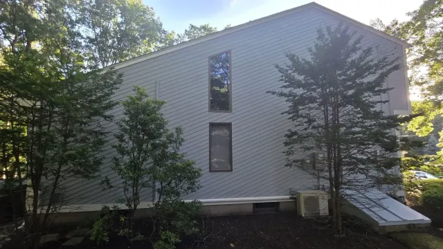 White-sided house exterior with trees and a small ramp along the right side.