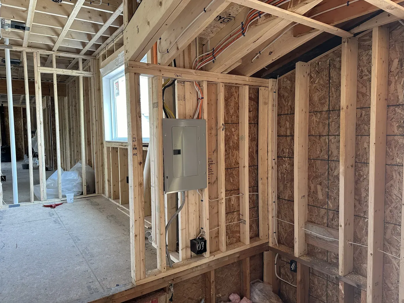 Electrical panel and circuit wiring run through the open stud framing of a house under construction