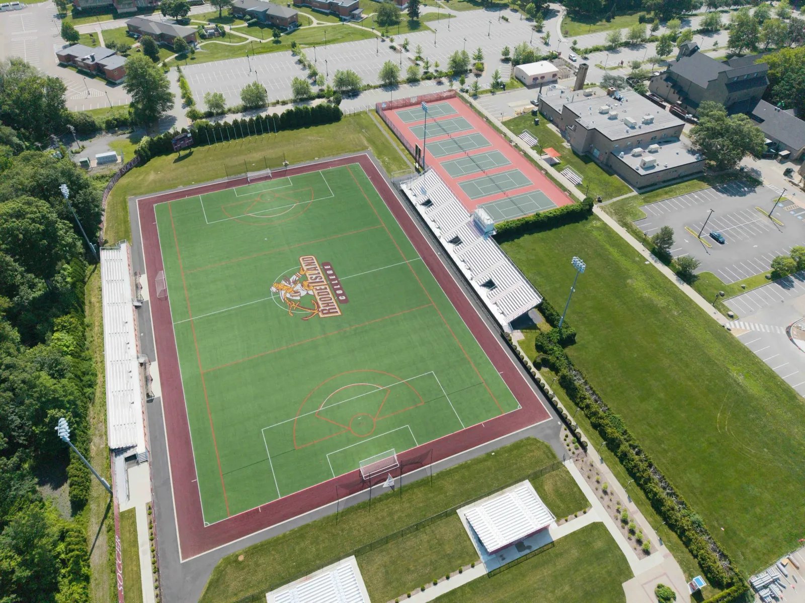 Aerial view of a sports complex with a football field at Kansas City Royals, a tennis court, parking lots, and nearby residential and commercial buildings.