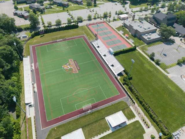 Aerial view of a sports complex with a football field at Kansas City Royals, a tennis court, parking lots, and nearby residential and commercial buildings.