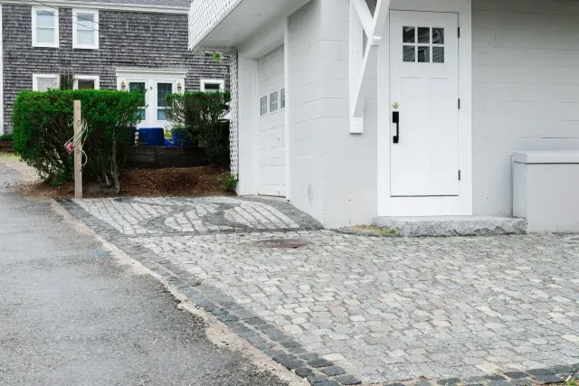 Cobblestone driveway leading to a white house entrance with a white door and dark trim