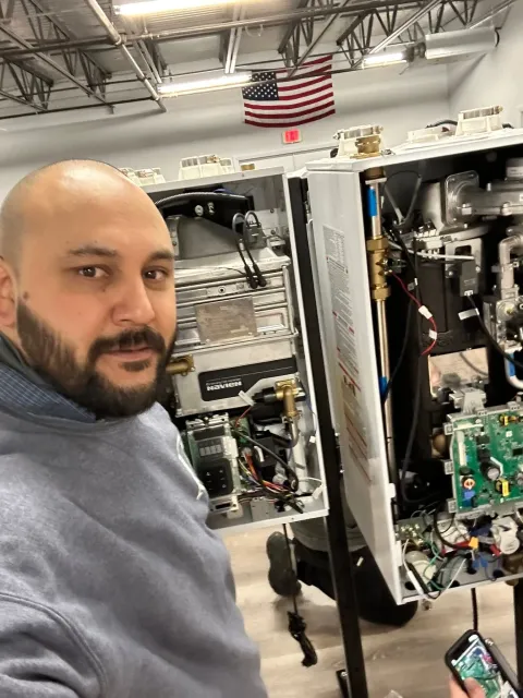 Person taking a selfie beside open electronics equipment in a workshop, with an American flag in the background.
