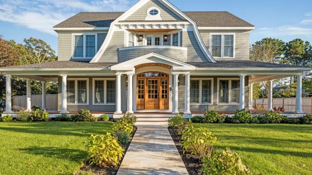 Landmark gray house with white trim and wraparound porch, set by lush lawn under blue sky – McPhee Associates of Cape Cod.