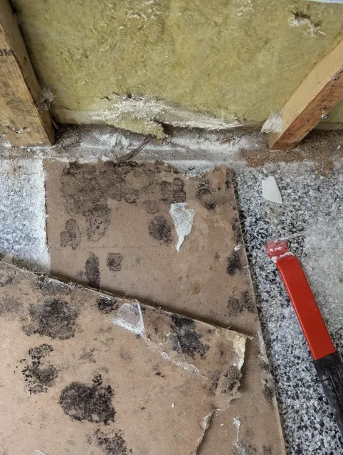 Close-up of insulation material and debris on a construction floor, with a red tool handle visible in the bottom right corner.