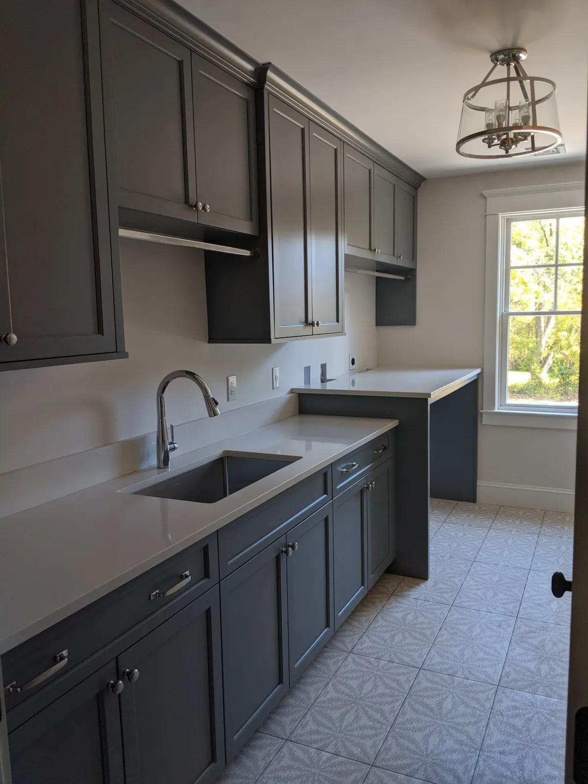 Kitchen with gray cabinets, white countertops, a stainless steel sink, and a window showing outdoors with trees.
