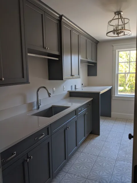 Kitchen with gray cabinets, white countertops, a stainless steel sink, and a window showing outdoors with trees.