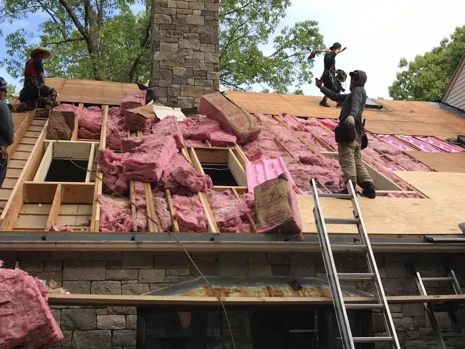 Roofers working on a roof, removing insulation. Pink insulation and wood structure visible.