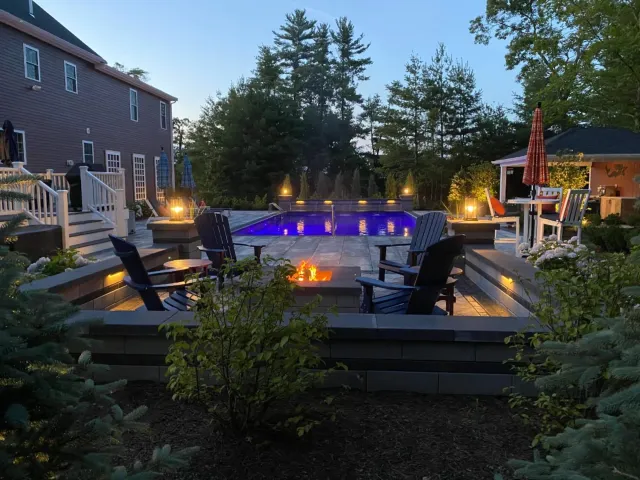 Landscape design at night, large patio with in-ground pool and lit fire pit