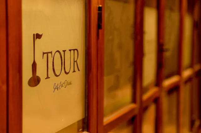 A row of books on a shelf, with the closest book titled 'TOUR' with a wine glass icon and the phrase 'Golf. Eat. Drink.' visible on the cover.