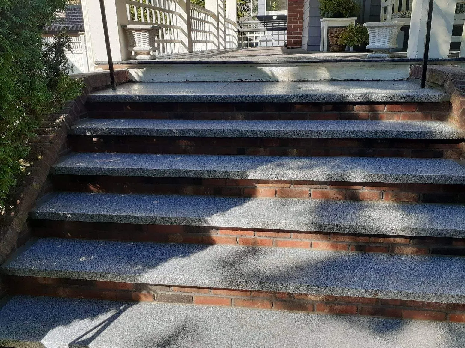 Brick steps with dark railings and sunlight shadows leading up to a house entrance