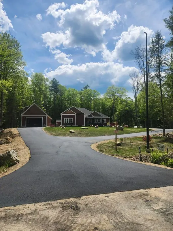 Asphalt driveway leading to a brown house and detached garage on a sunny day.