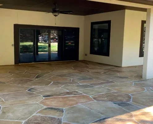 Covered patio with flagstone-style flooring, dark-framed sliding doors, and a ceiling fan.