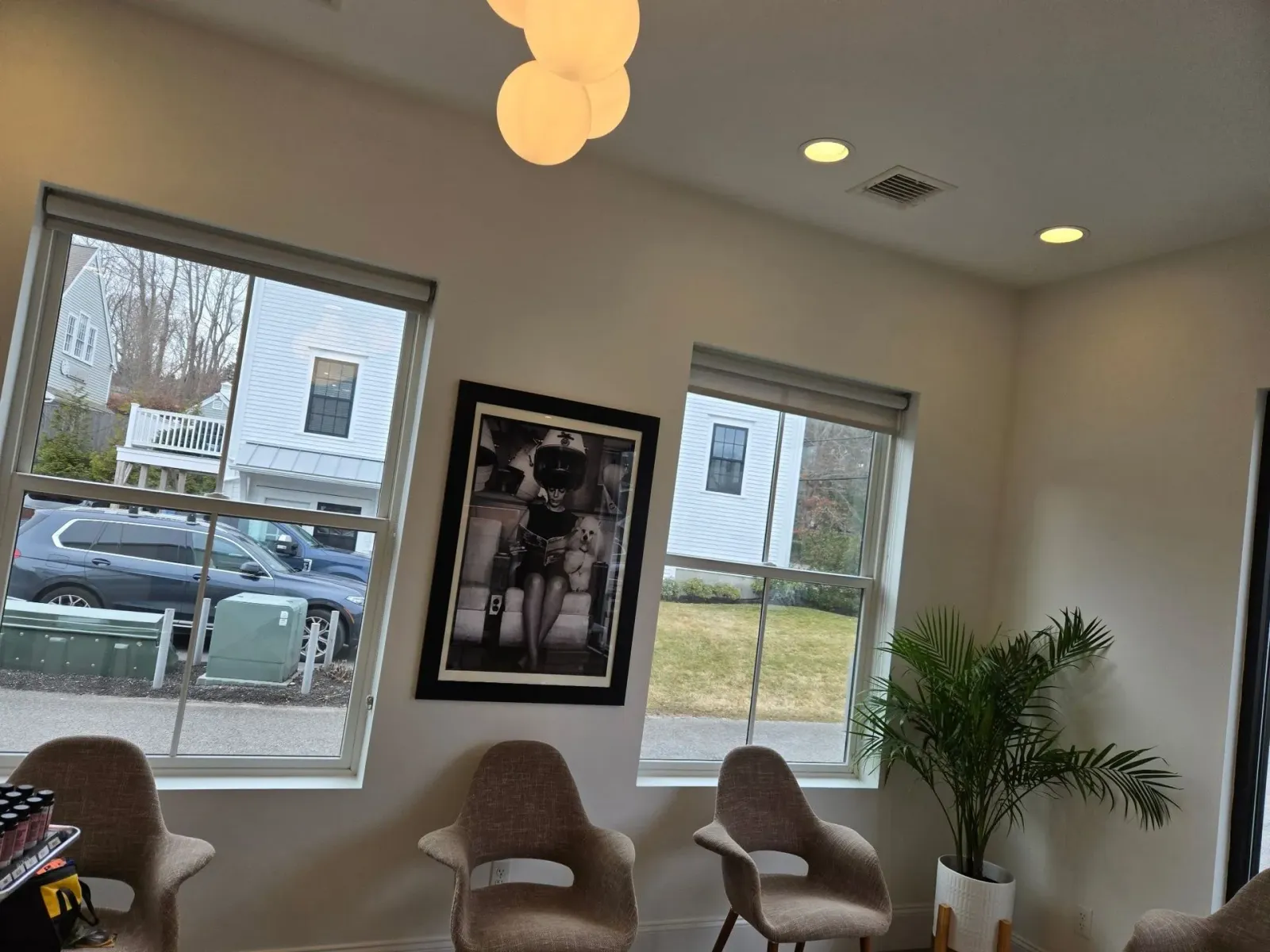 Modern waiting room with chairs, windows, framed wall art, ceiling lights, and a potted plant.