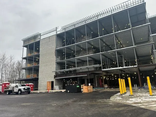 Building under construction with steel framework, grey brick, and a concrete entrance. Cloudy day.
