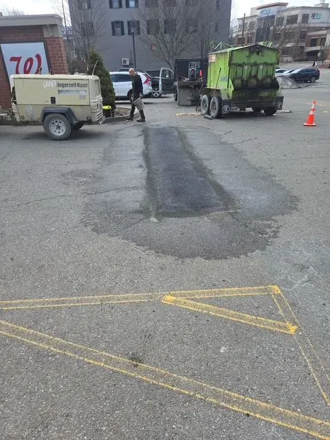 Two utility trucks and workers patching a road pothole, with cones marking the area.