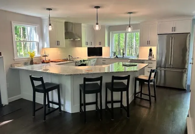 Modern kitchen with white cabinets, island with stools, stainless steel appliances, and dark wood floors.