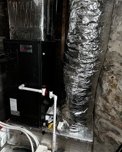 a black air conditioner is sitting next to a duct in a basement