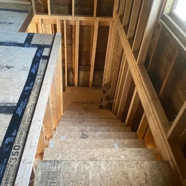 Interior staircase under construction with exposed wooden framing and OSB steps