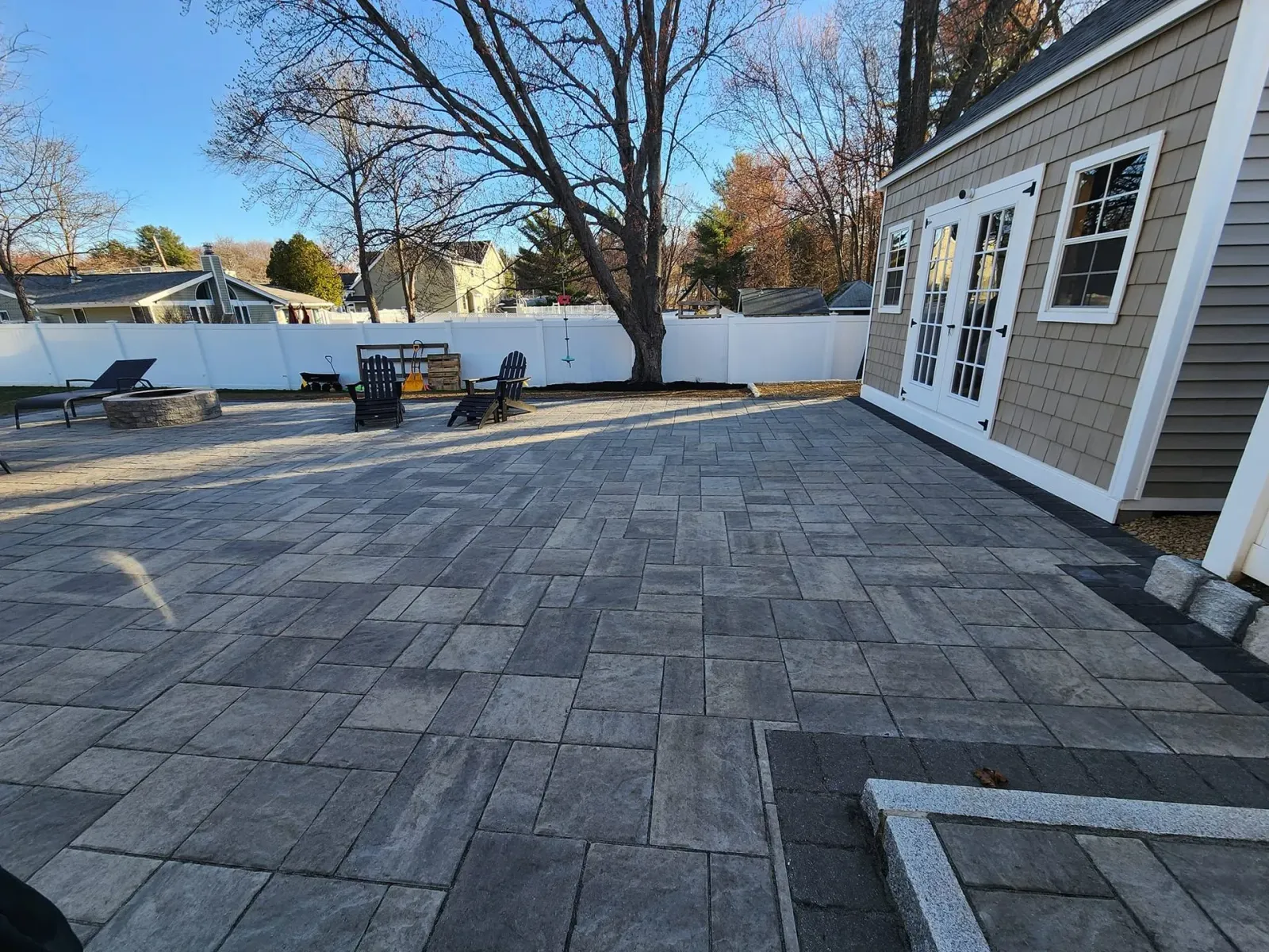 Large paver patio with shed, fire pit, and fence in a backyard setting.