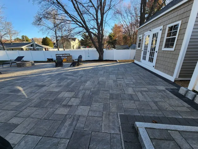 Large paver patio with shed, fire pit, and fence in a backyard setting.